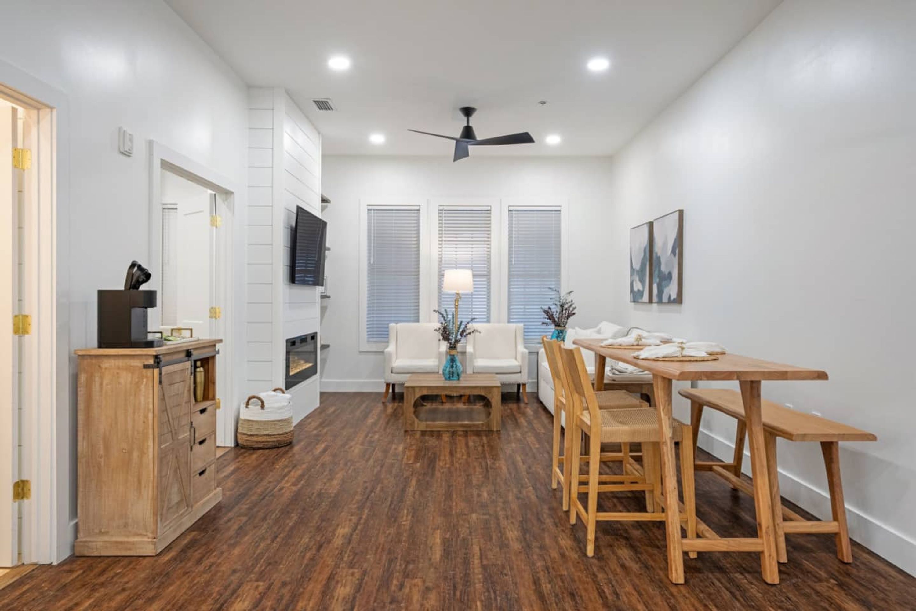 Una sala de estar moderna con una mesa de comedor de madera, sofás blancos y un televisor montado en la pared.