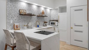 A modern kitchen with a white marble island, built-in microwave, and a herringbone-patterned backsplash.