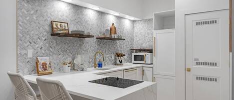 A modern kitchen with a white marble island, built-in microwave, and a herringbone-patterned backsplash.