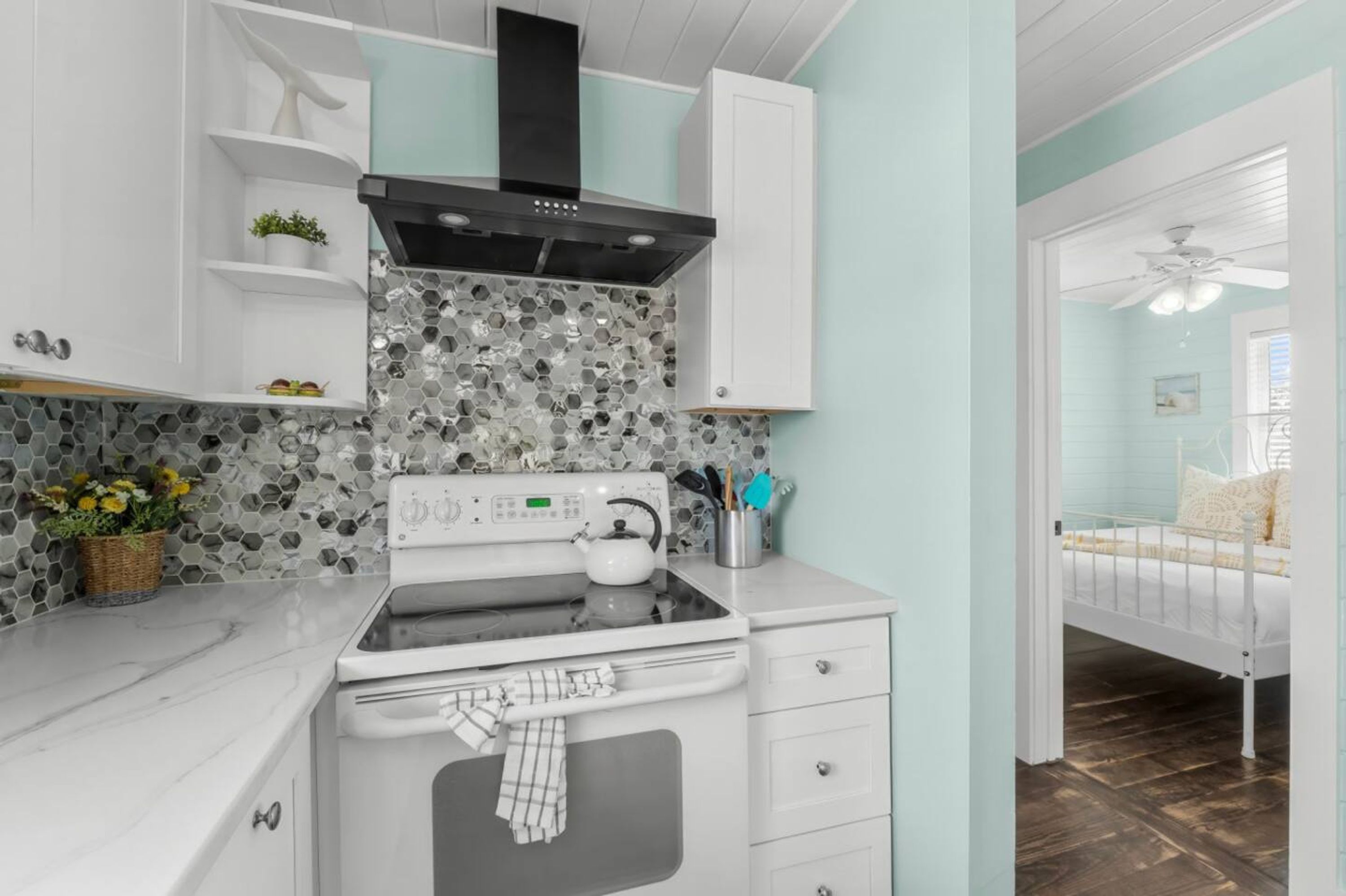 A kitchen with a stove, oven, and white cabinets. There is a window with a view of the outside.