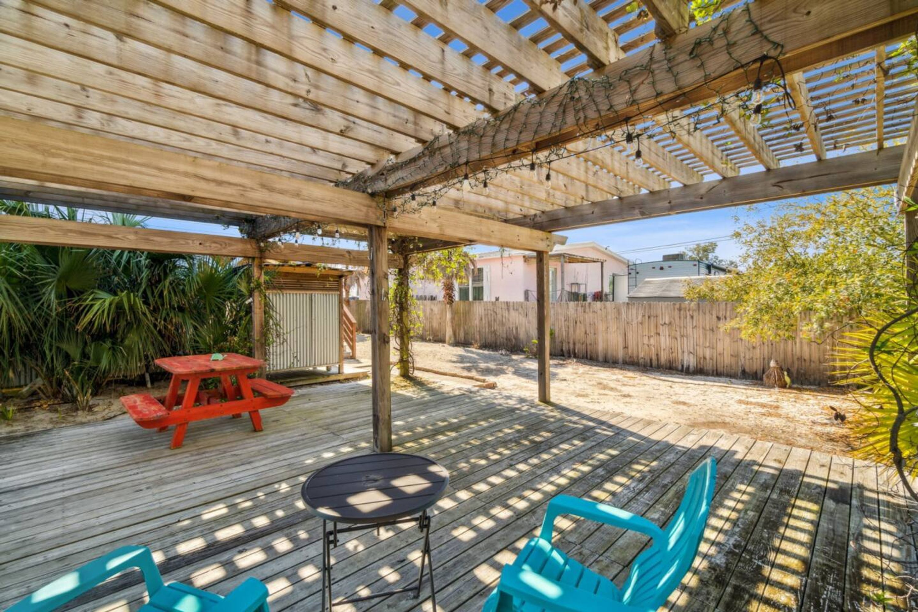 A wooden deck with a pergola, a red picnic table, and blue chairs.