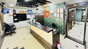 Zona de recepción con mostrador, sillas, televisor montado en la pared y un espejo que refleja la sala.