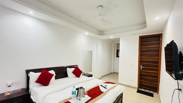 Una habitación de hotel con una cama grande, una mesita de noche, un televisor montado en la pared y una puerta de madera.