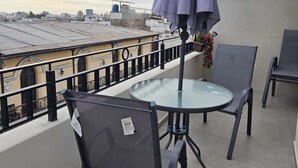 Una terraza en la azotea con una mesa redonda de cristal y dos sillas, un paraguas morado y una farola.