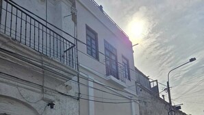 Un edificio de dos pisos con fachada blanca, un balcón en el nivel superior y un cerrojo cerrado en la planta baja.