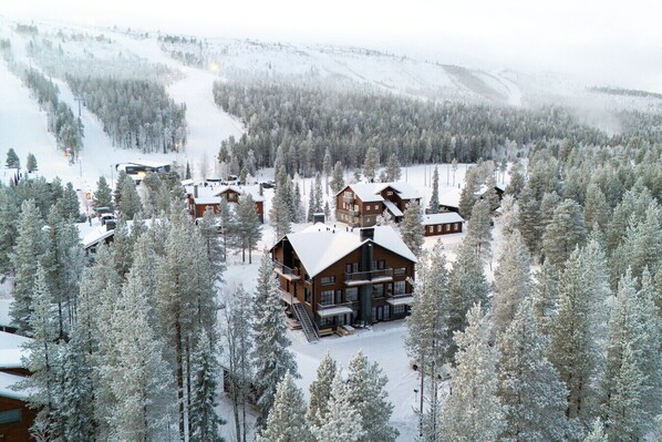 A lodge with multiple buildings surrounded by snow-covered trees, set in a mountainous area.