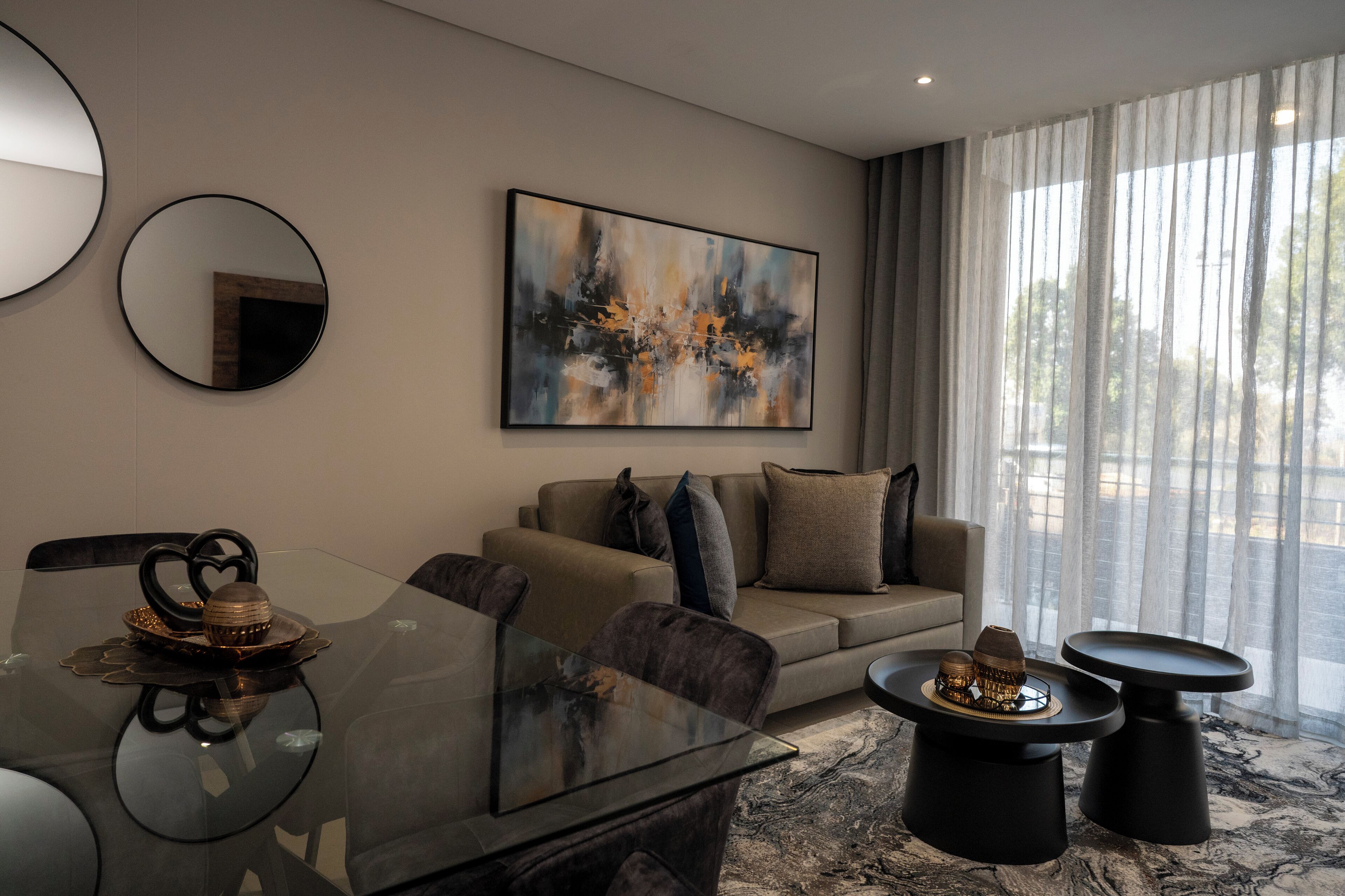 A modern living room with a glass dining table, a sofa, and two side tables.