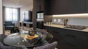 A modern kitchen with dark cabinetry, a glass dining table, and a built-in oven. - Lux Leisure Apartment Hotel Sandton (Sandton)