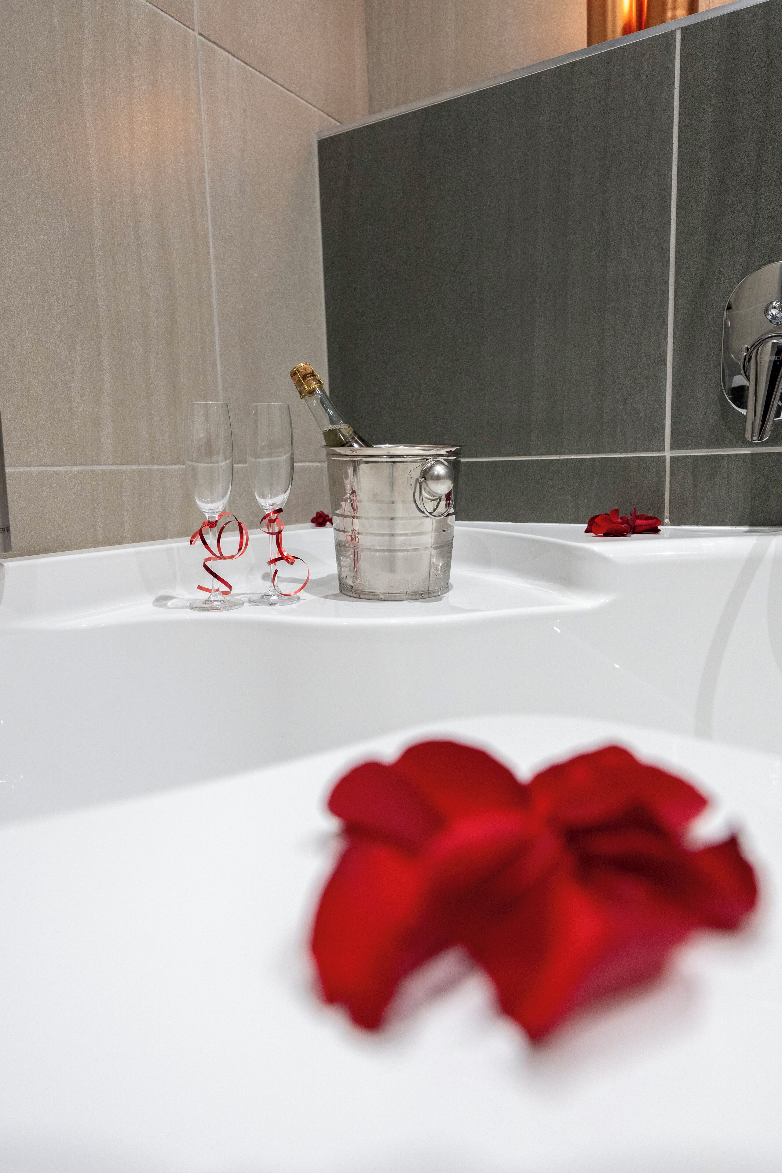 A bathroom with a white sink, a champagne bucket, two glasses, and a red rose.