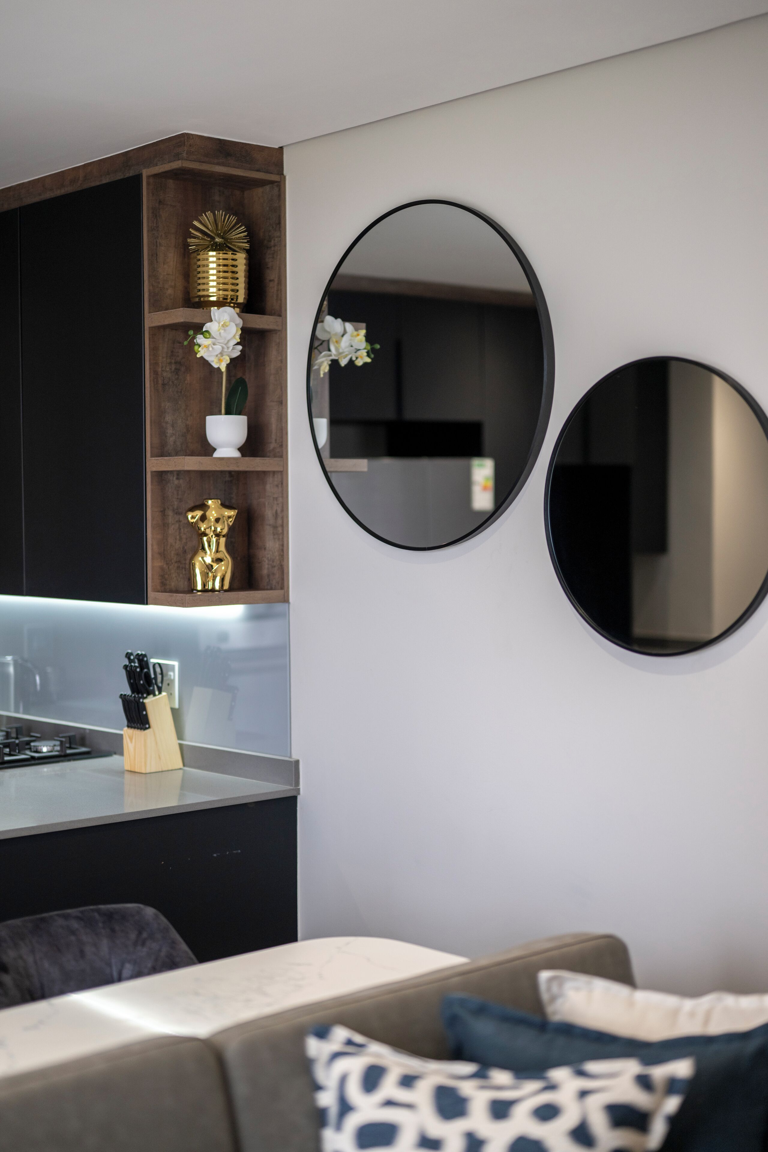 A modern kitchen with dark cabinetry, a wooden shelf with decorative items, and a built-in stove.