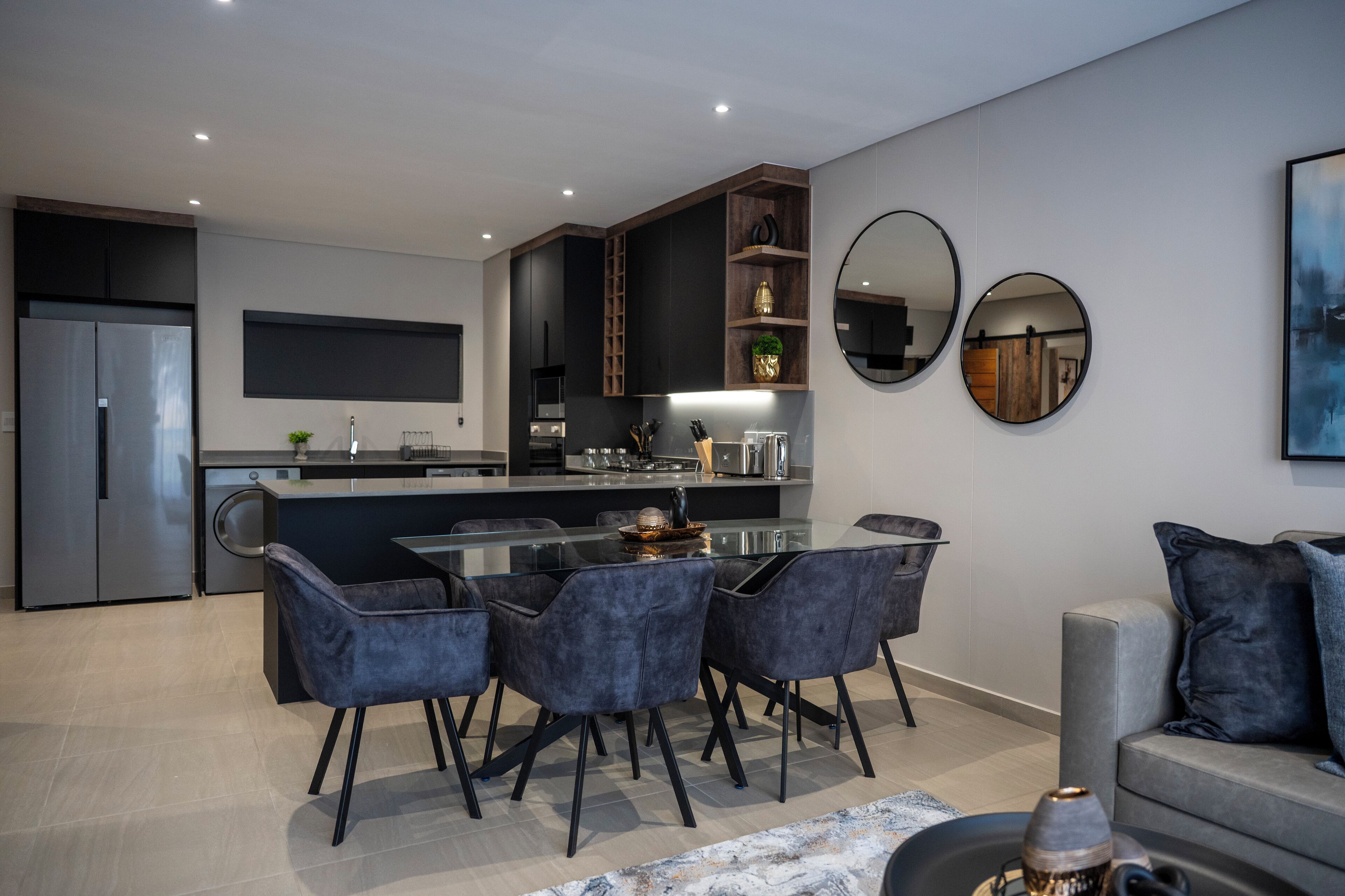 A modern kitchen with a central island, dark cabinetry, and a dining area with chairs.