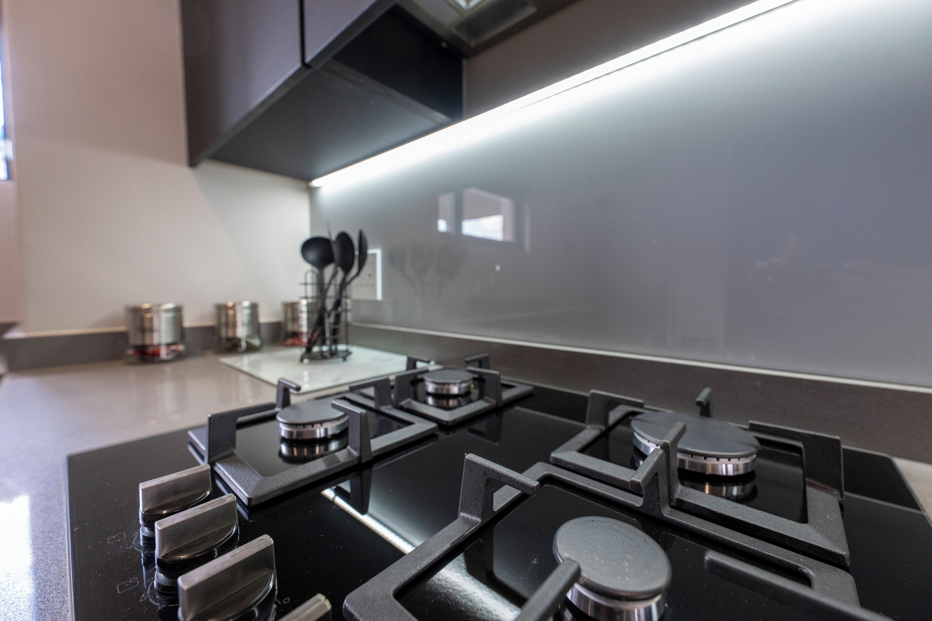 A modern kitchen with a black stove top, stainless steel handles, and a backsplash.