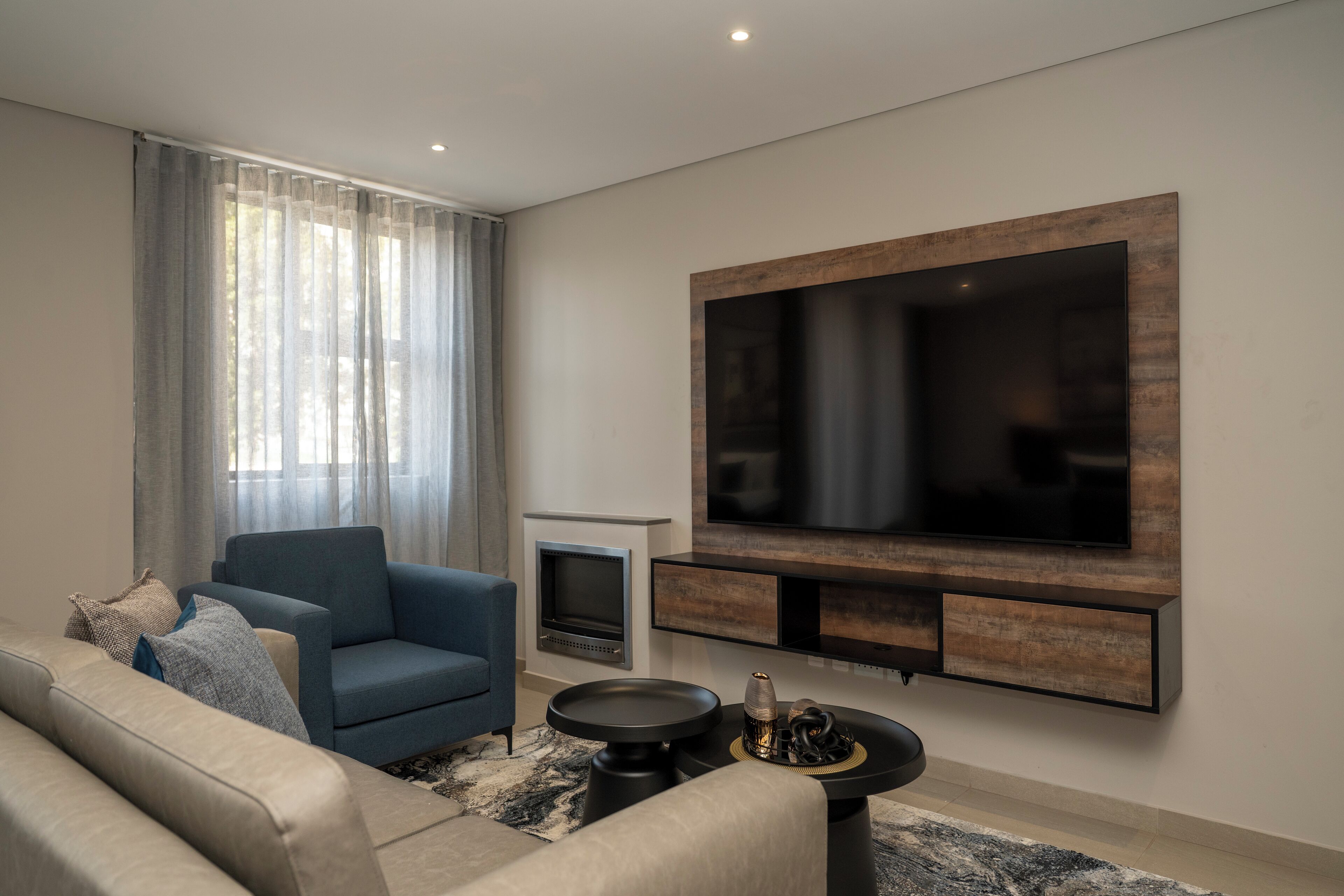 Una sala de estar moderna con un sofá, una mesa de centro, una chimenea y un televisor de pantalla plana grande montado en la pared.