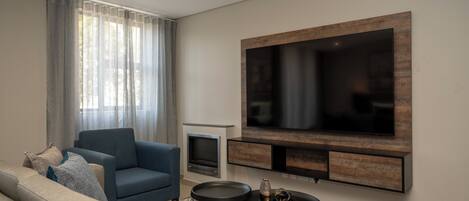 Una sala de estar moderna con un sofá, una mesa de centro, una chimenea y un televisor de pantalla plana grande montado en la pared.