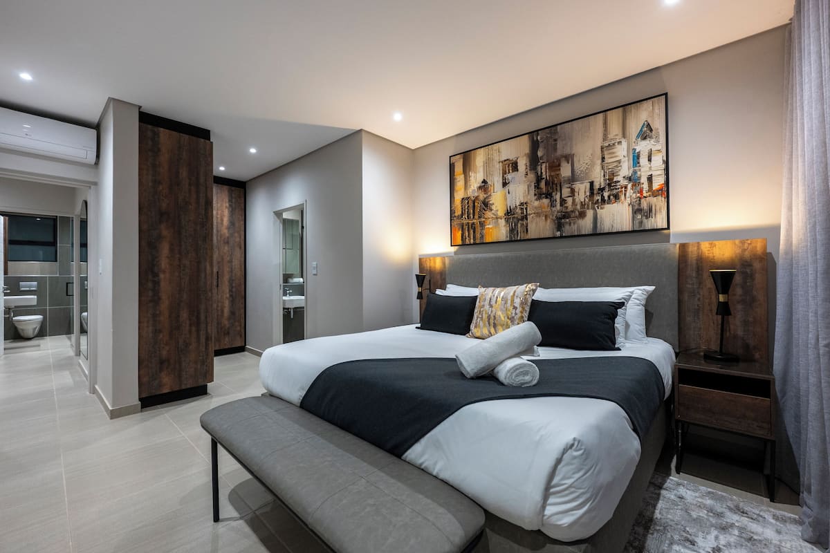 Una habitación de hotel moderna con una cama grande, un banco, un revestimiento de pared de madera y un cuadro de un paisaje urbano.
