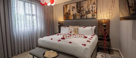 A modern bedroom with a large bed, a bench, and a cityscape painting.