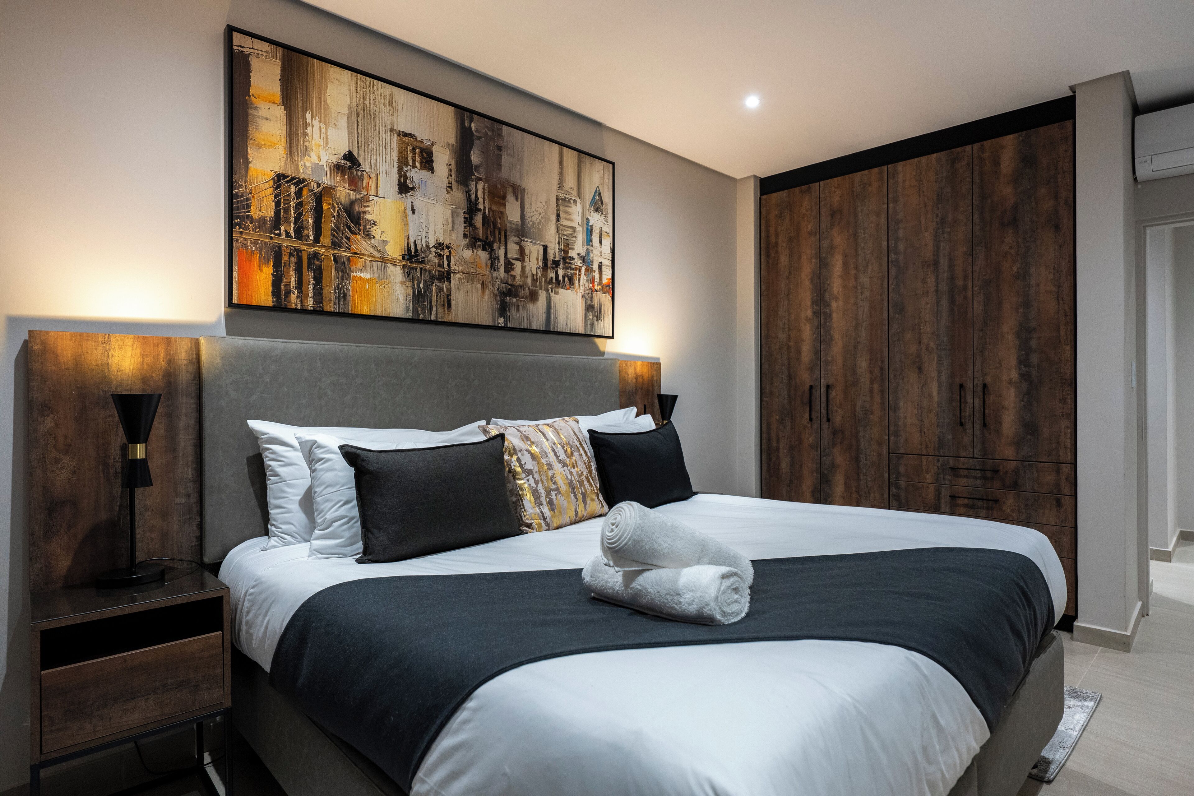 A modern bedroom with a large bed, a headboard, bedside tables, and a large abstract painting on the wall.
