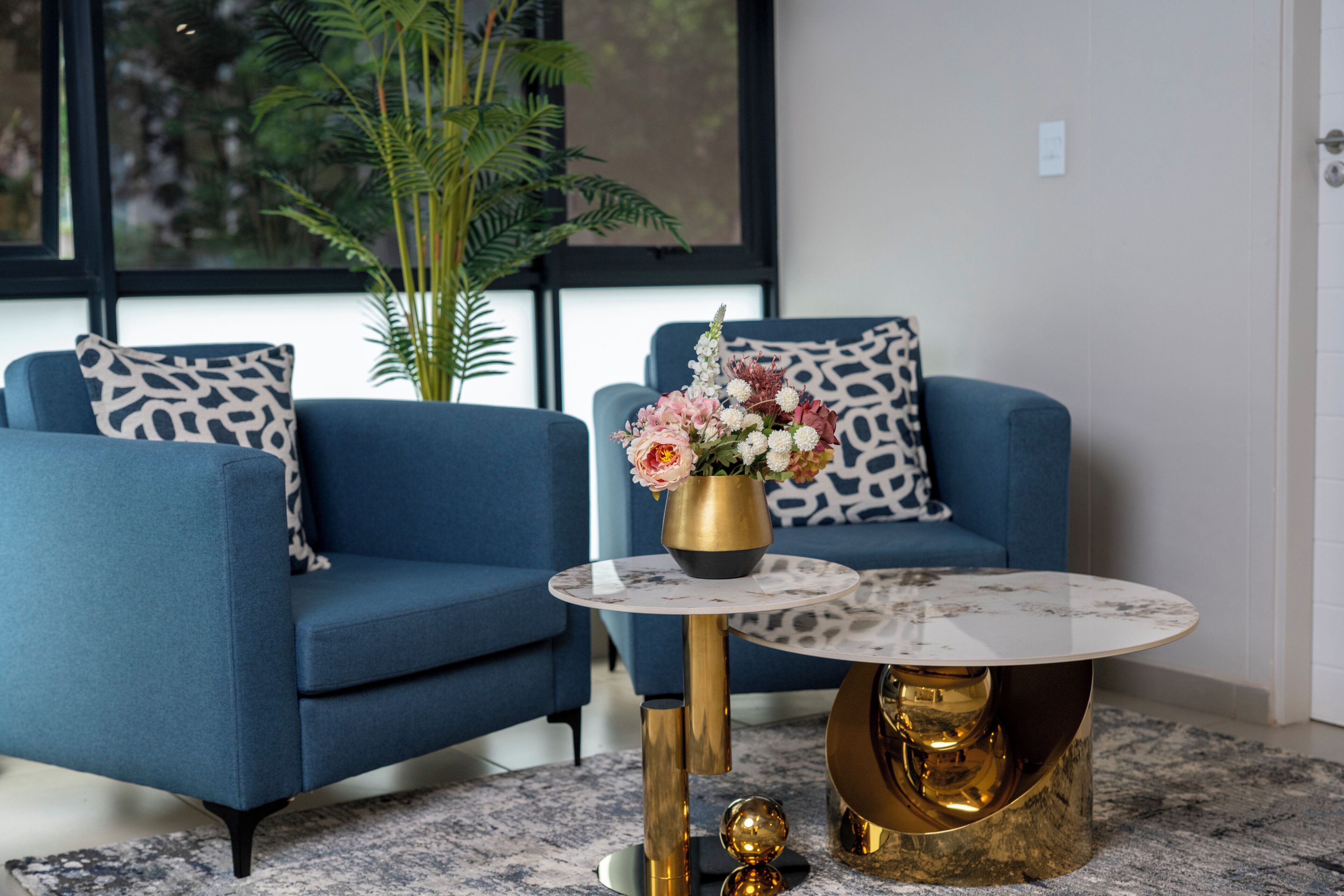 A modern living room with a blue sofa, a round coffee table with a gold base, and a potted plant.