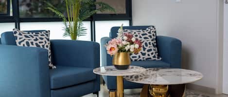 A modern living room with a blue sofa, a round coffee table with a gold base, and a potted plant.