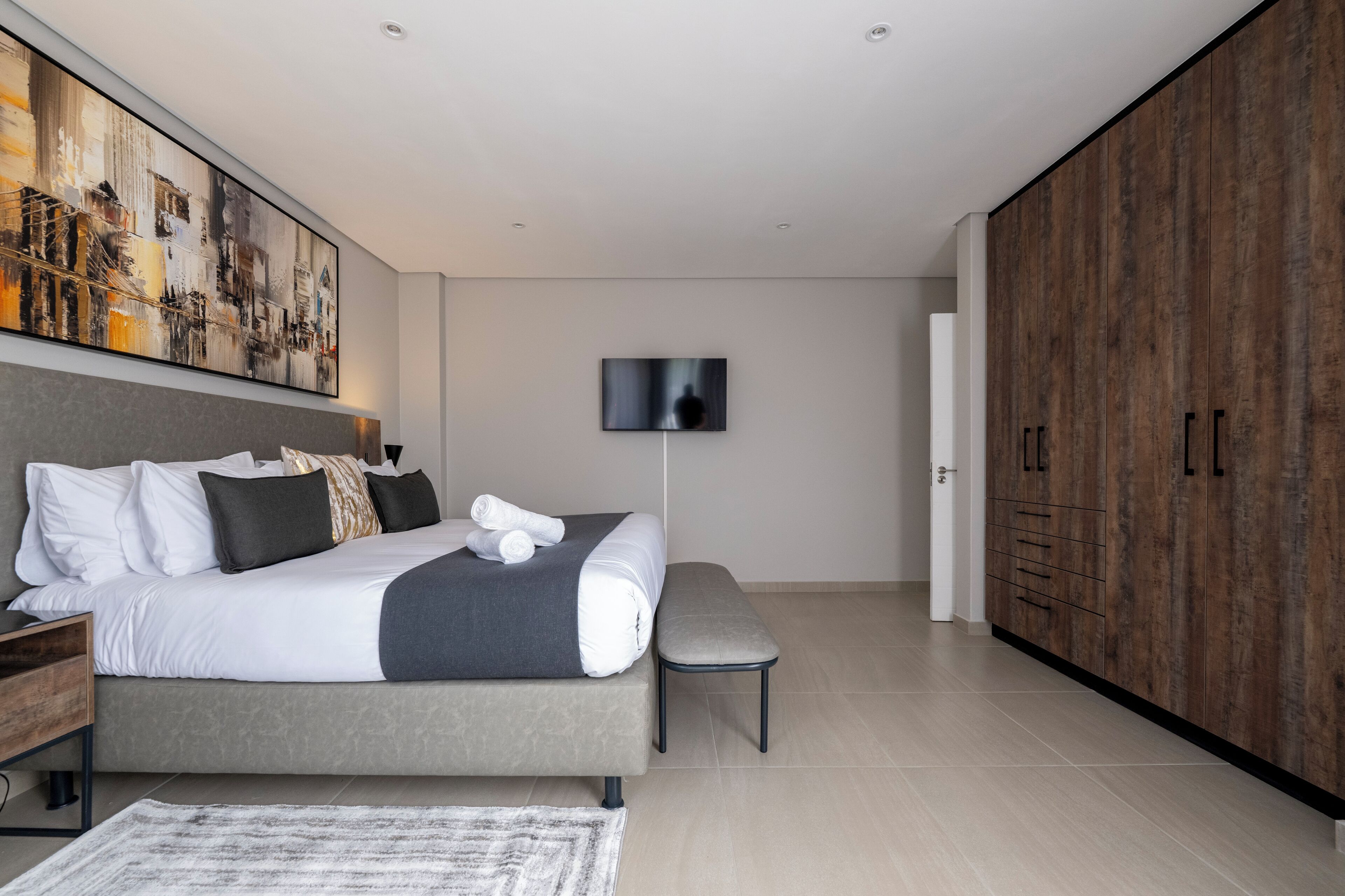 Une chambre moderne avec un grand lit, un téléviseur à écran plat, une armoire et un tableau au mur.