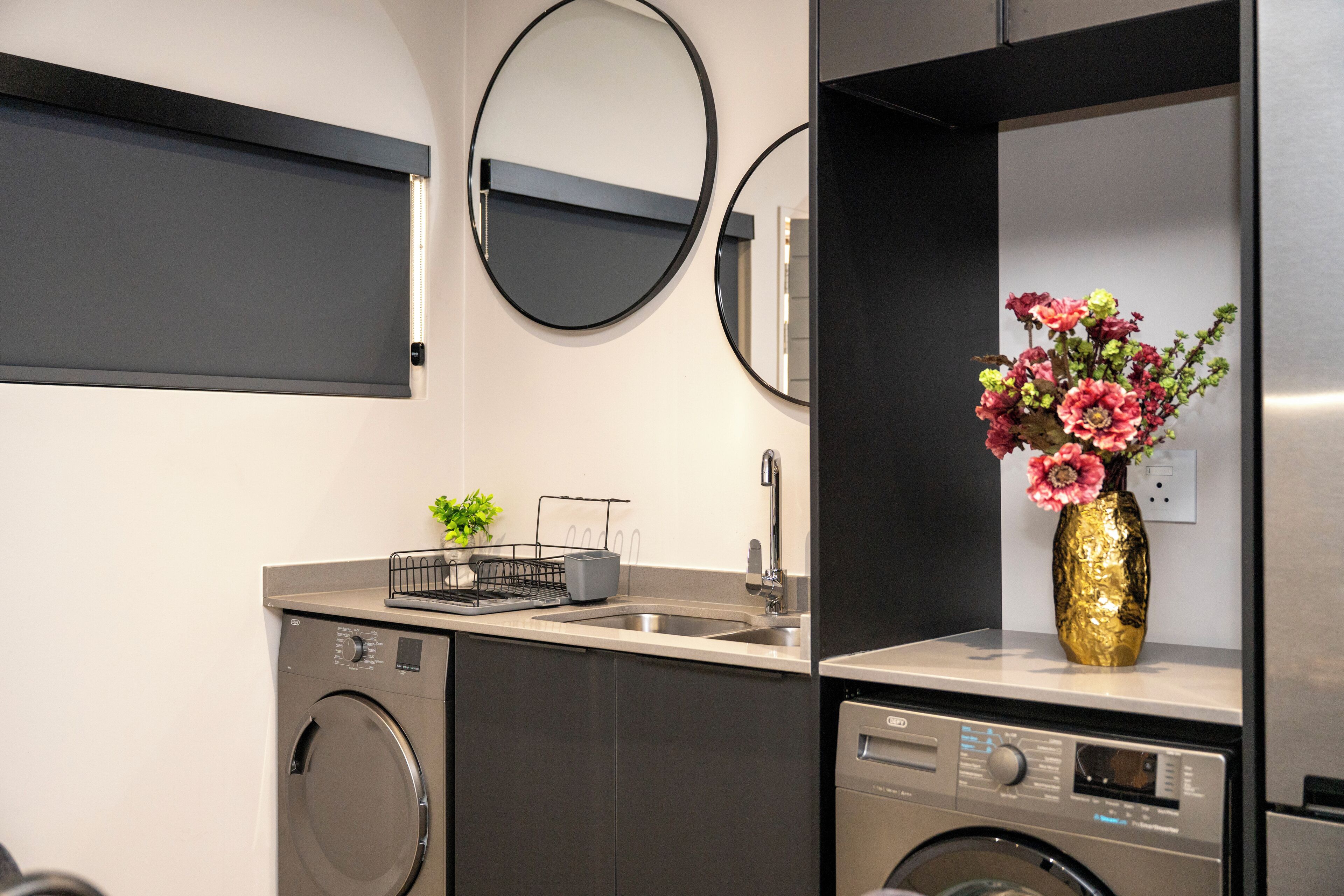 A compact kitchen with a washing machine, a sink, and a vase with flowers.