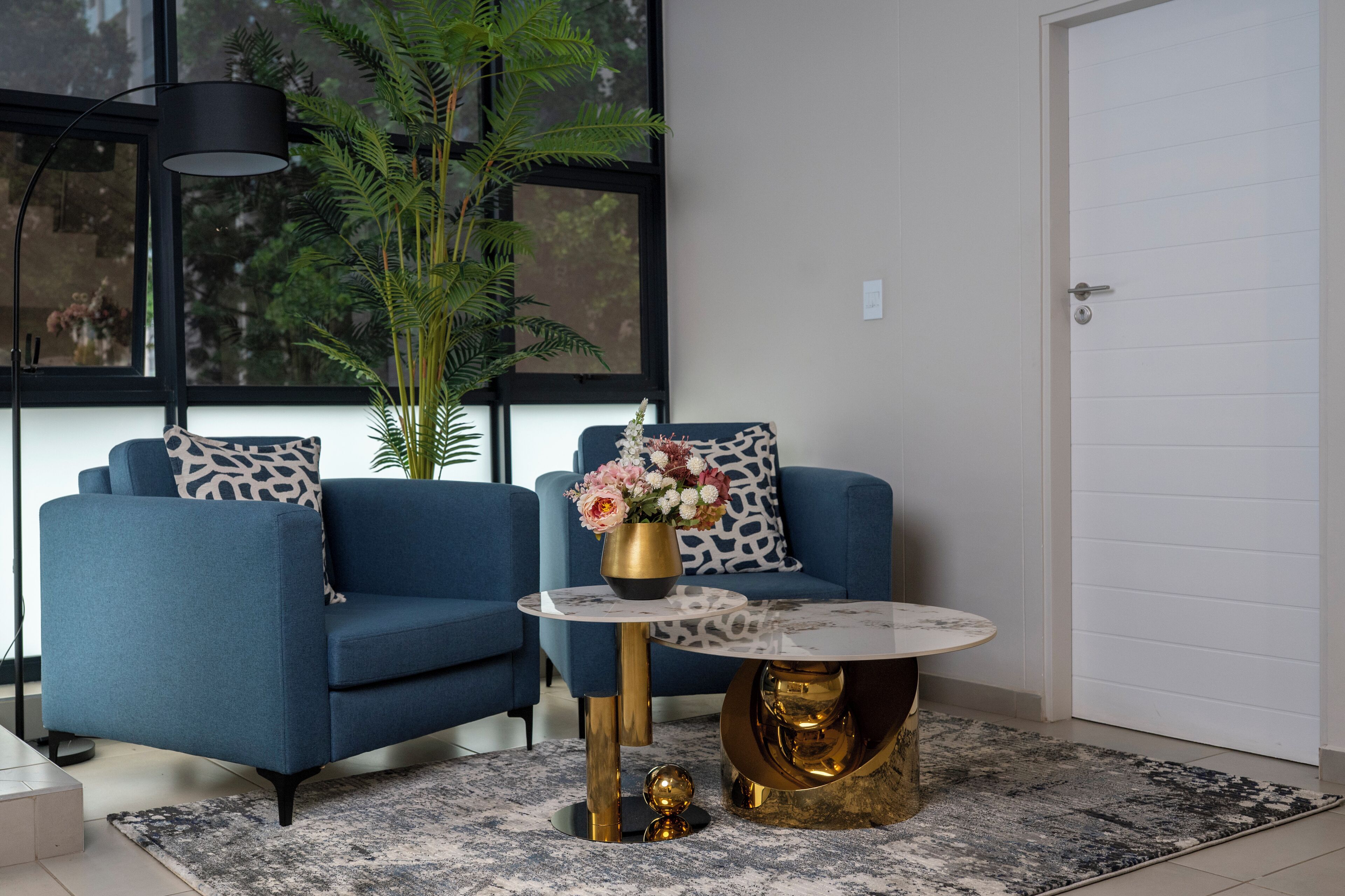 A modern living room with a blue sofa, a round coffee table, and a large window with a view of trees.