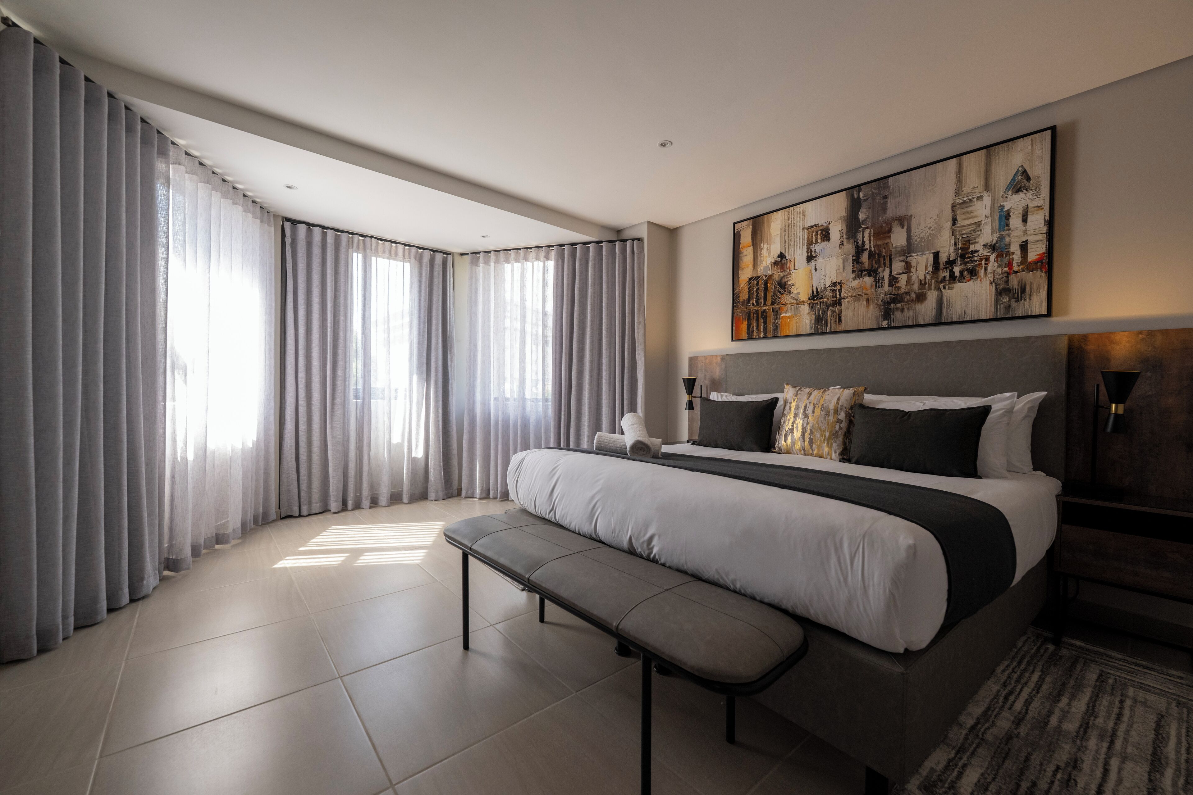 A modern hotel room with a large bed, a bench, and a painting on the wall.