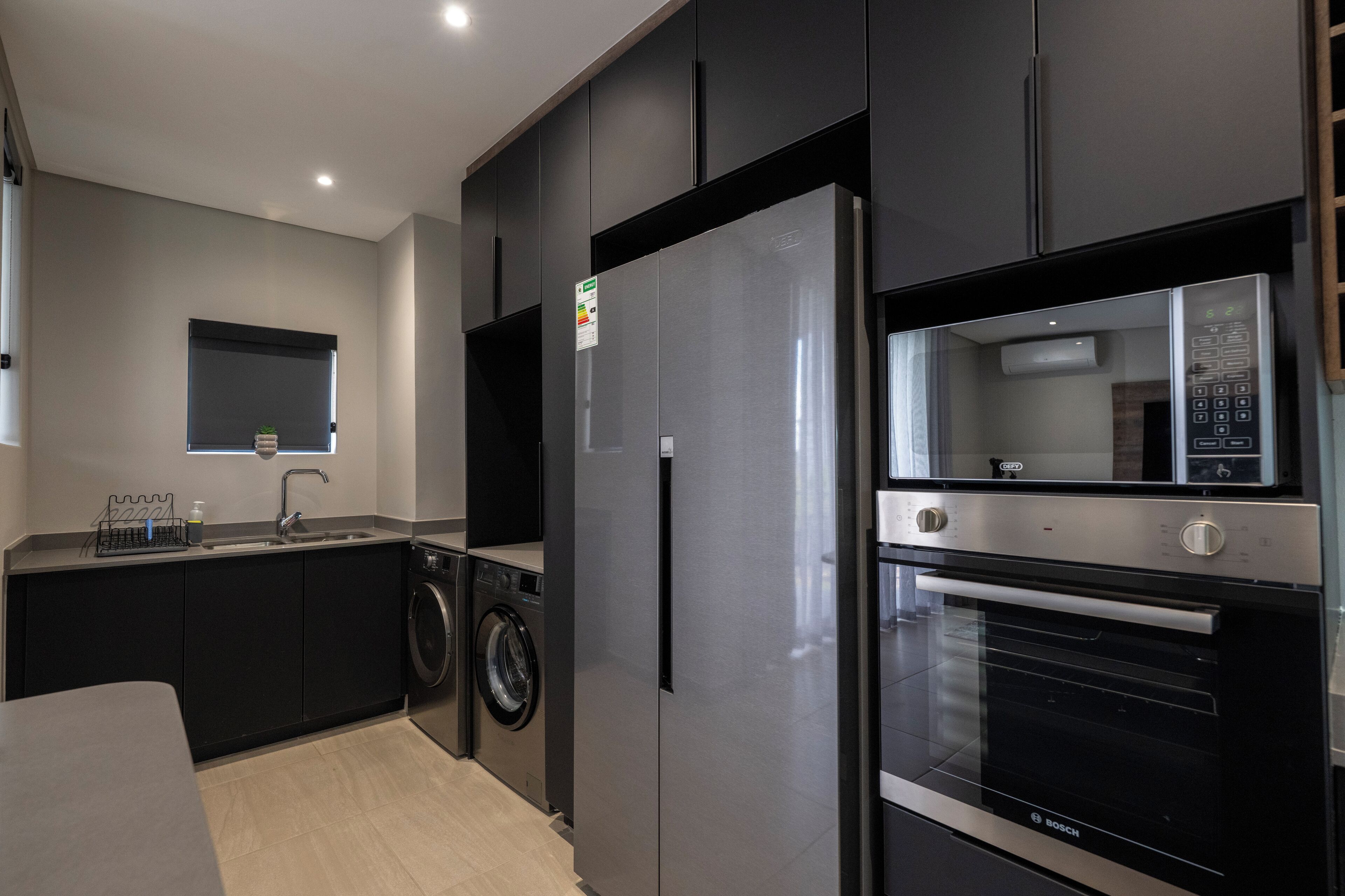A modern kitchen with a built-in washing machine, a stainless steel refrigerator, and a Bosch oven.