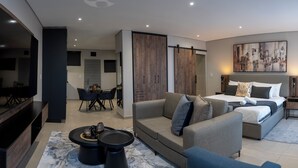 A modern hotel room with a large bed, a sofa, a TV, and a dining area. - Lux Leisure Apartment Hotel Sandton (Sandton)