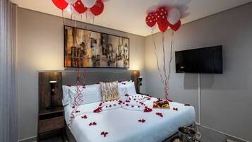 A hotel room with a bed, a TV, and a painting on the wall.
