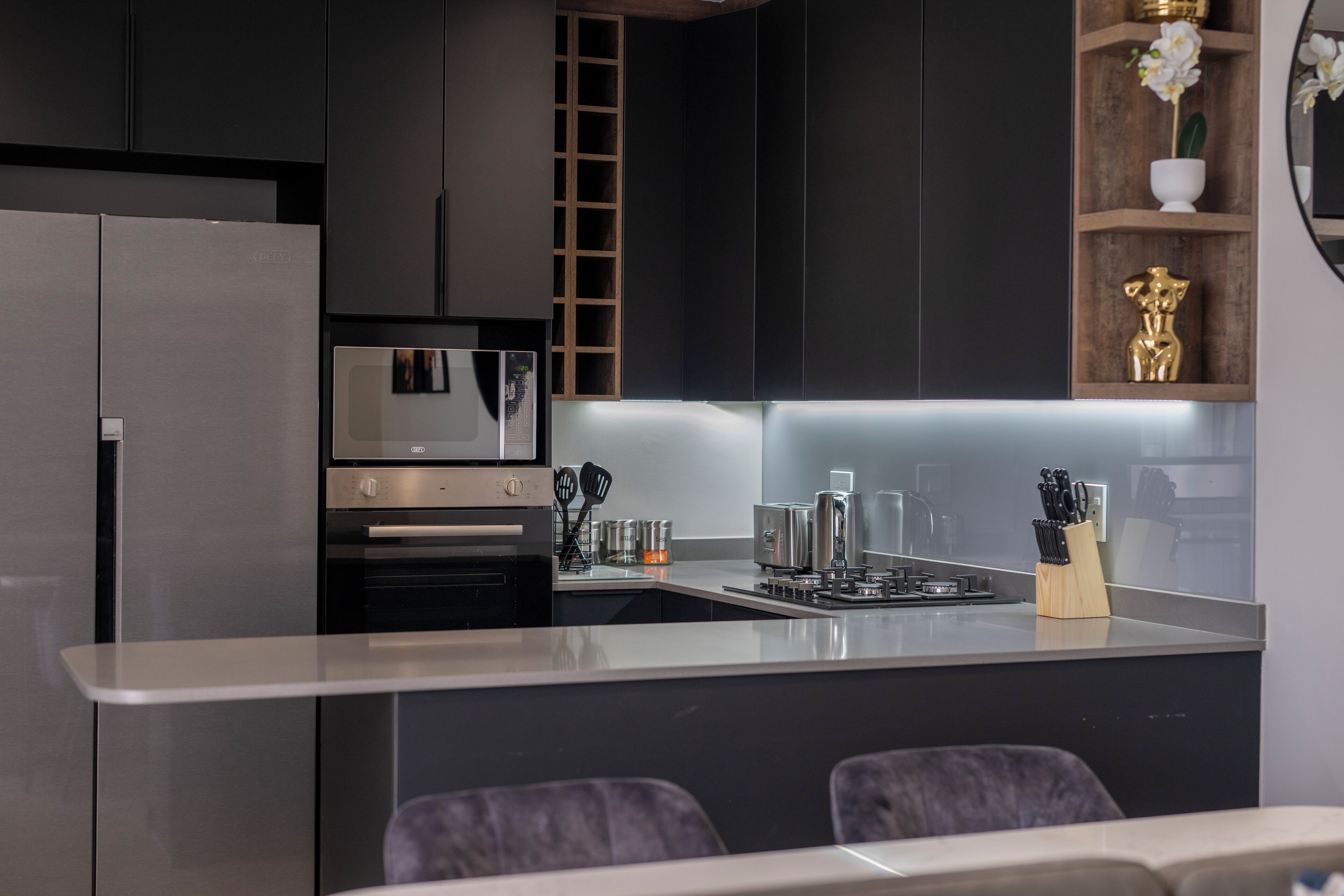 A modern kitchen with dark cabinetry, a stainless steel refrigerator, a microwave, and a central island with a sink and knife block.