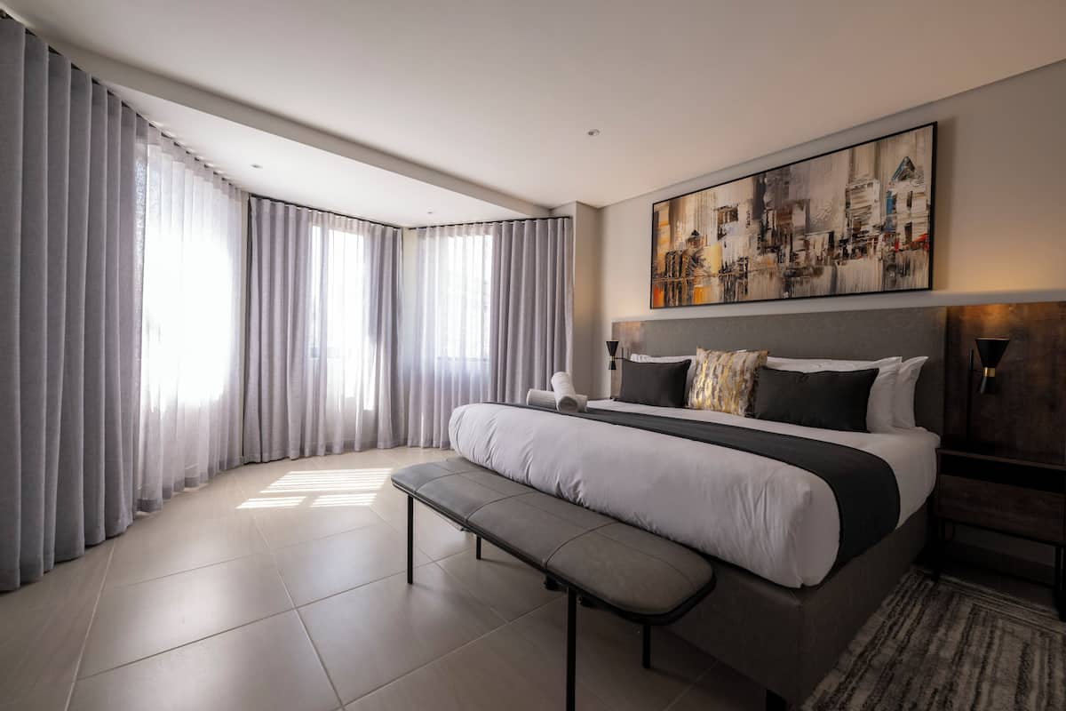 Un dormitorio moderno con una cama grande, un banco y un cuadro de un paisaje urbano en la pared.