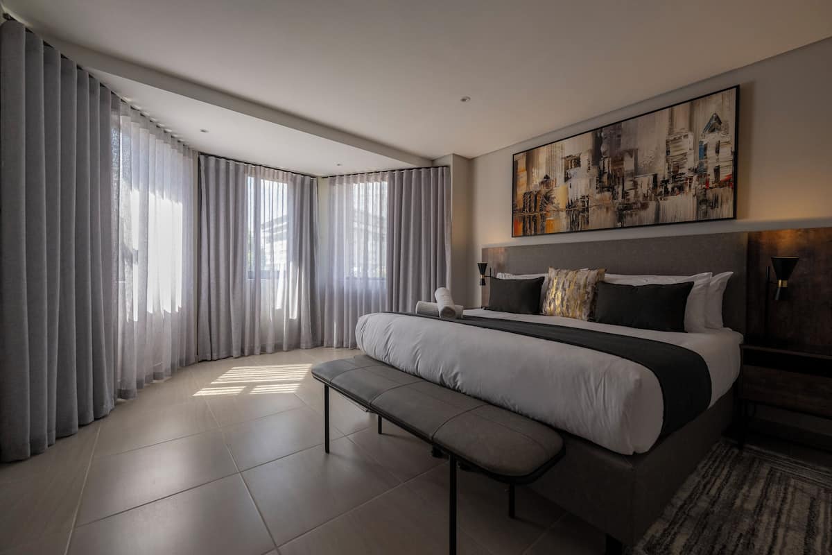 Una habitación de hotel moderna con una cama grande, un banco y un cuadro de un paisaje urbano en la pared.