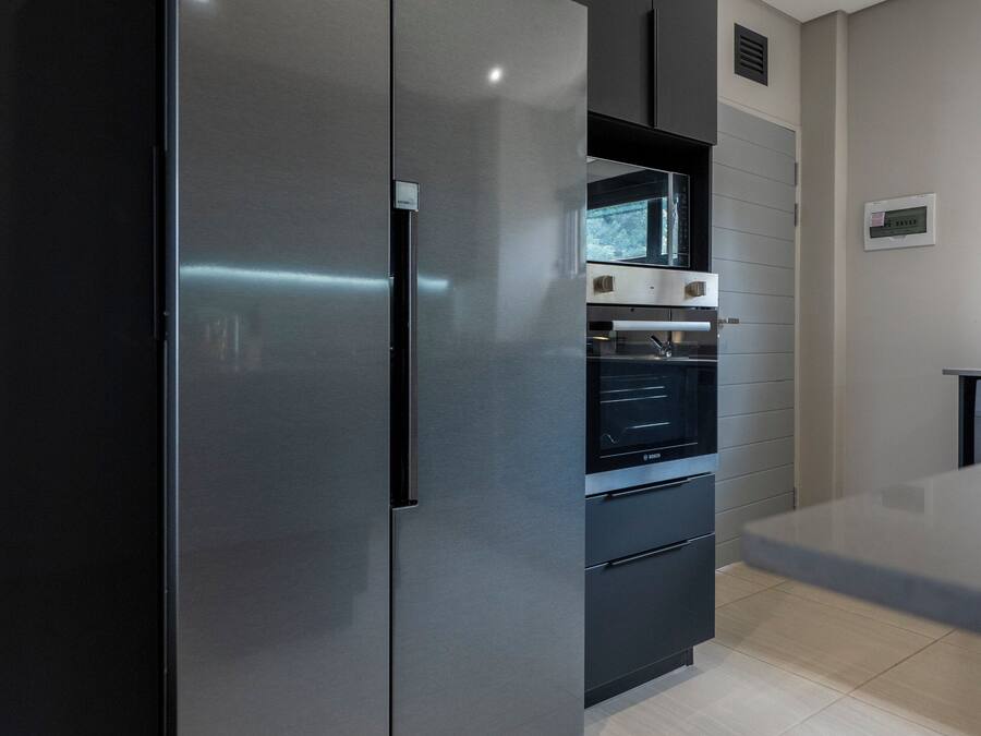 A modern kitchen with a large stainless steel refrigerator, built-in oven, and dark cabinetry.
