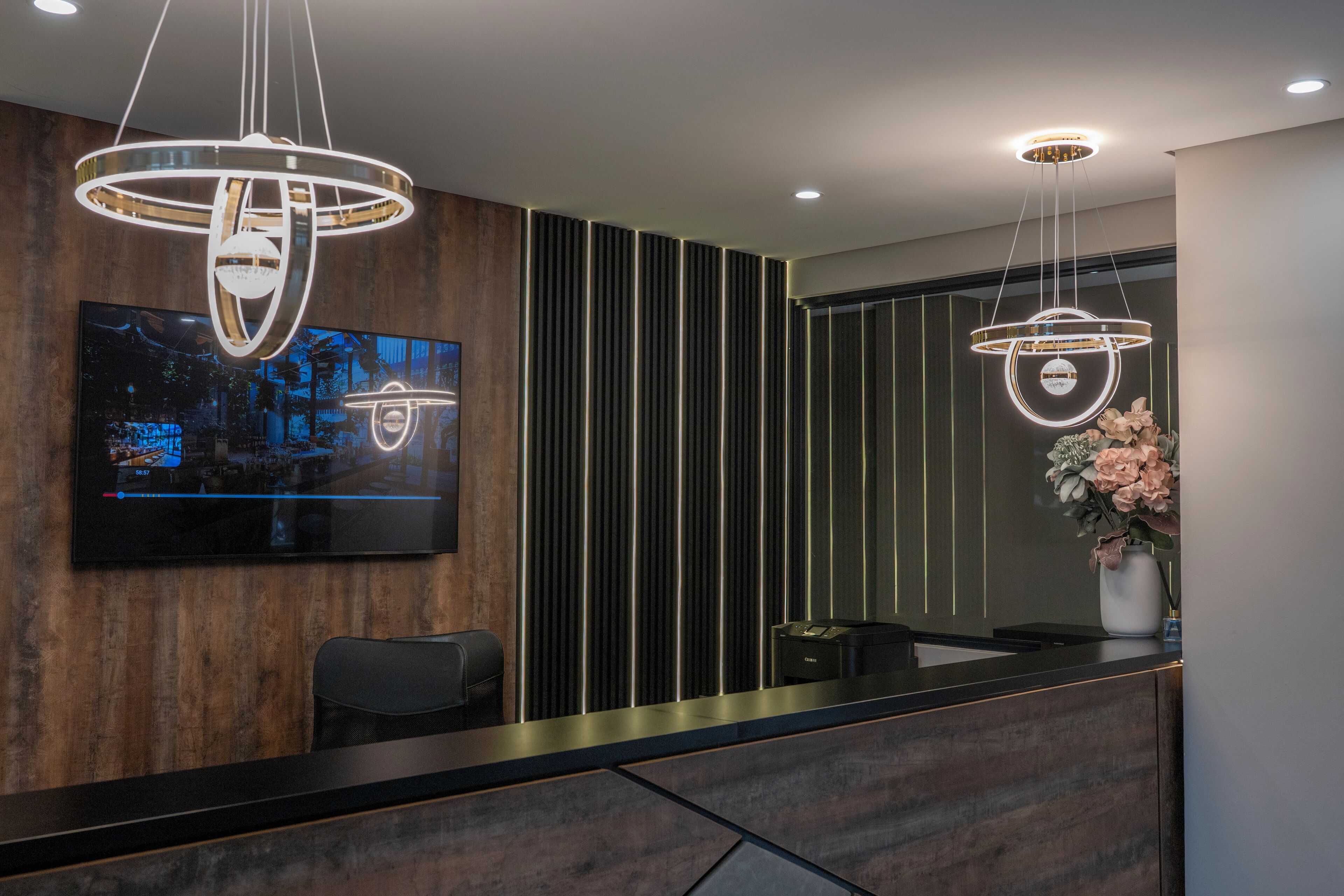 A modern reception area with a wooden panel wall, a flat-screen TV, and two pendant lights.