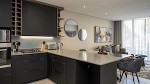 A modern kitchen with dark cabinetry, a central island, and a dining area with a sofa and chairs. - Lux Leisure Apartment Hotel Sandton (Sandton)