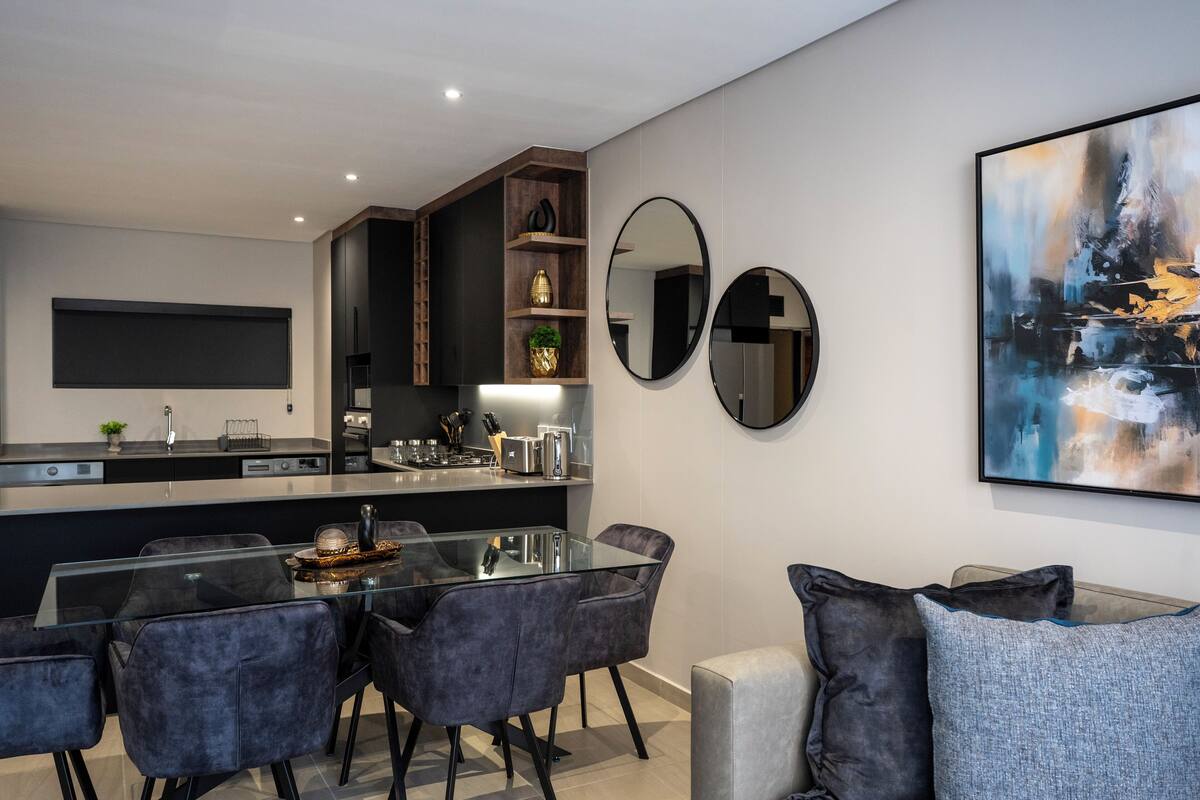 Una cocina moderna con una isla central, electrodomésticos integrados y un comedor con mesa y sillas de vidrio.