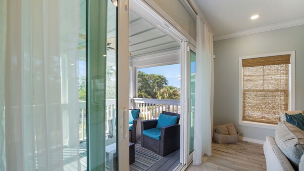 A room with a sliding glass door leading to an outdoor deck, a sofa with cushions, and a window with a blind. - Introducing The Barefoot Villa in Lost Key! For An Upscale-Coastal Vacation. (Pensacola)