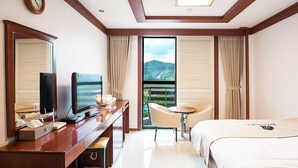 A hotel room with a bed, a desk with a television, a chair, and a view of a mountain through the window. - Benikea Hotel CheongDo Hot Spring (Cheongdo)