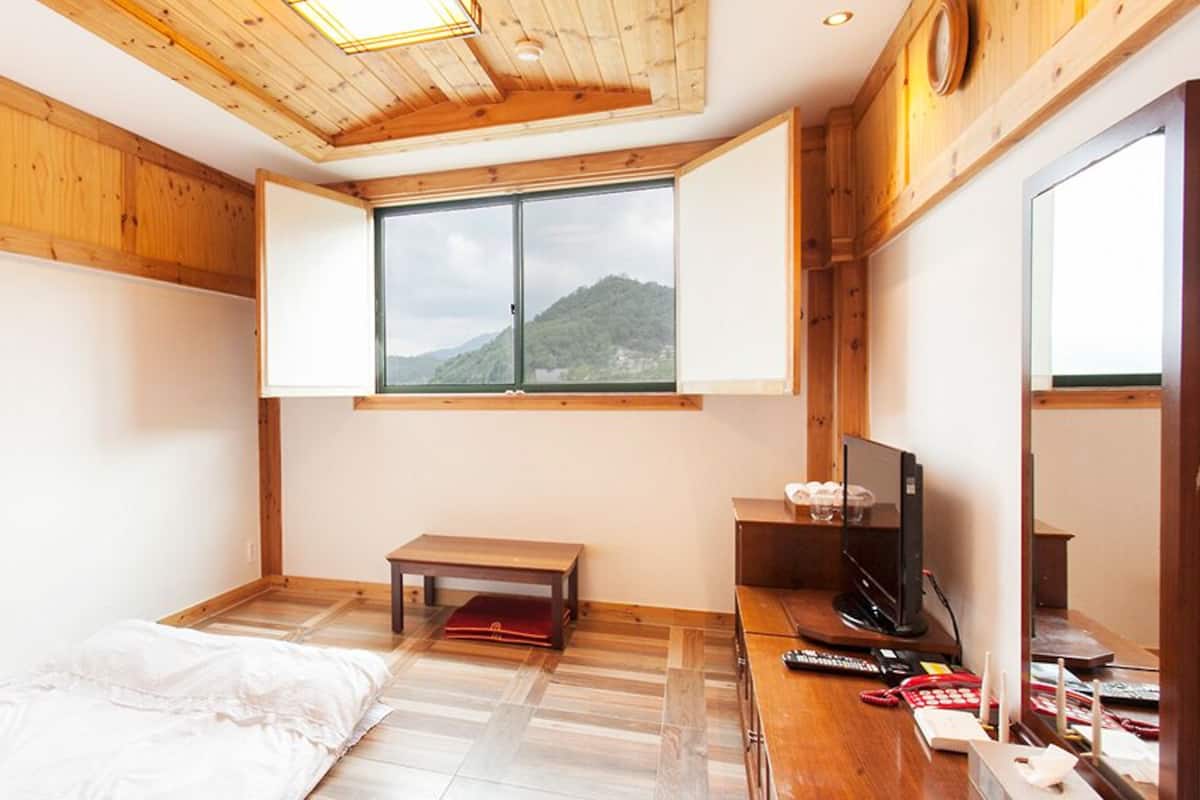 Ein Schlafzimmer mit Bett, kleinem Tisch, Fernseher und Fenster mit Blick auf die Berge.