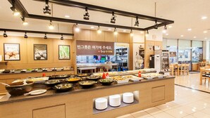 A buffet-style restaurant with a variety of food items displayed on a counter, a kitchen area in the background, and several dining tables and chairs. - Benikea Hotel CheongDo Hot Spring (Cheongdo)