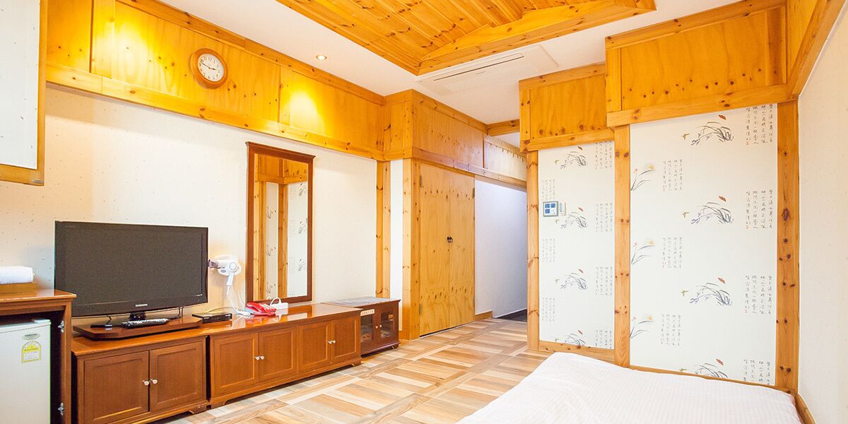 Una habitación con paredes de madera, una cama, un televisor, un armario y un espejo.