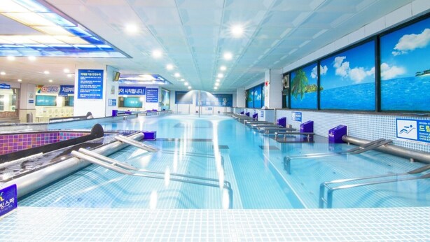 A large indoor swimming pool with multiple lanes, a reception area, and a view of the sea through large windows. - Benikea Hotel CheongDo Hot Spring (Cheongdo)