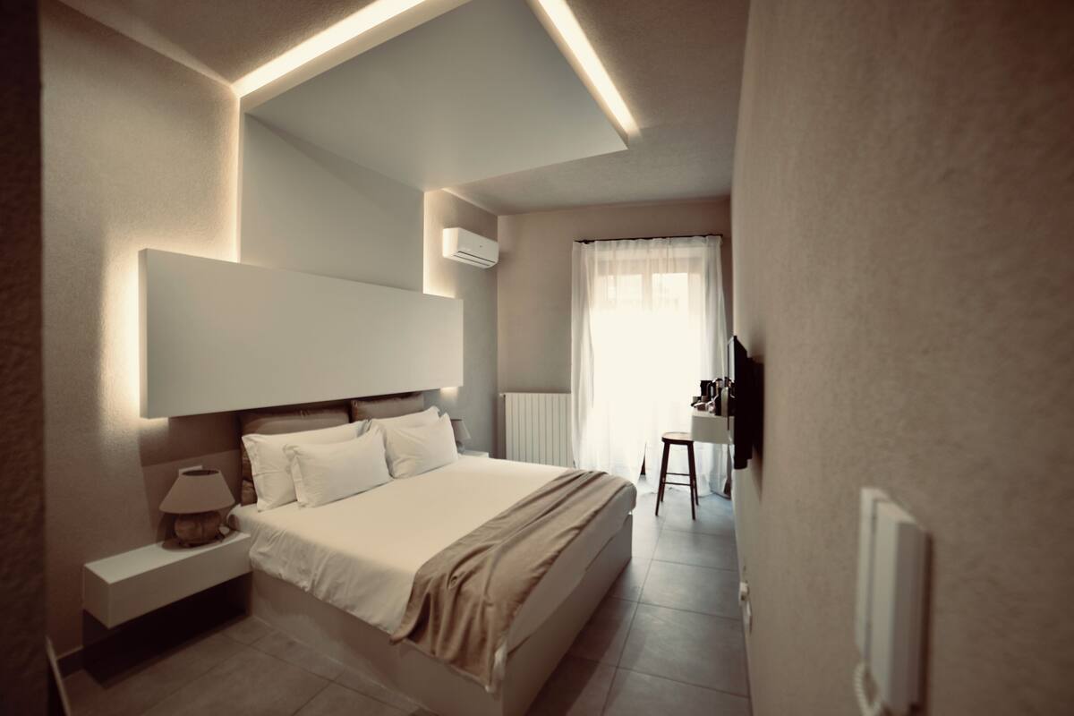 Una habitación de hotel moderna con una cama grande, mesita de noche, lámpara y vistas al baño.