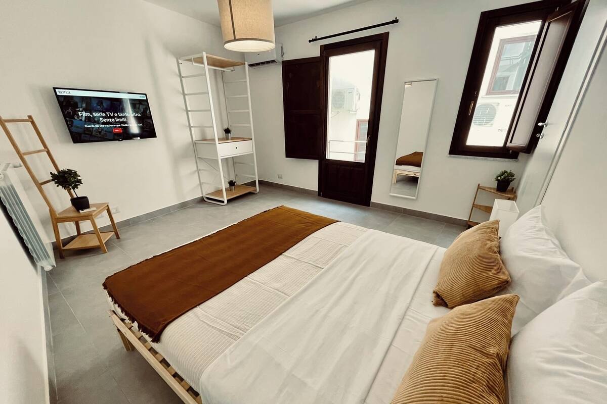 Un dormitorio moderno con una cama grande, un armario, un televisor y una ventana.