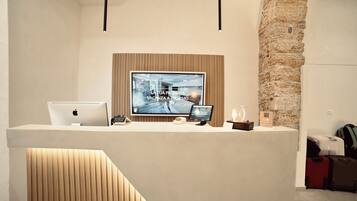 A reception desk with a flat-screen TV displaying a welcome message, a laptop, a tablet, and a smartphone.