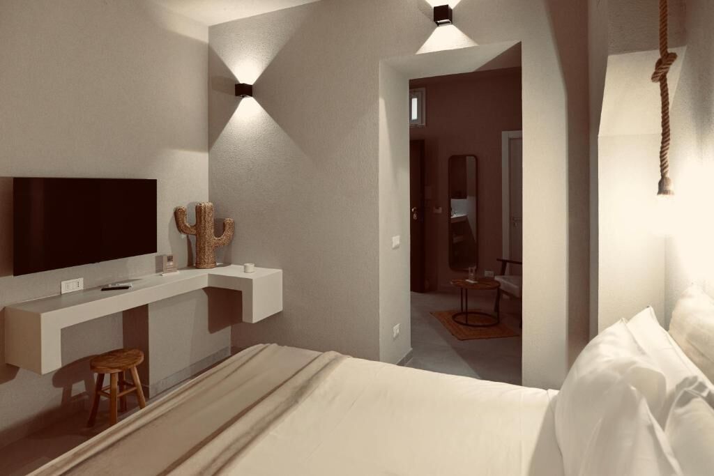 A modern hotel room with a large bed, a TV mounted on the wall, a small stool, and a unique cactus decoration.