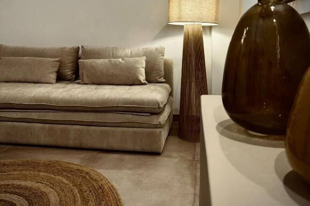 Una sala de estar moderna con un sofá color beige, una lámpara de pie y un jarrón grande sobre una mesa.