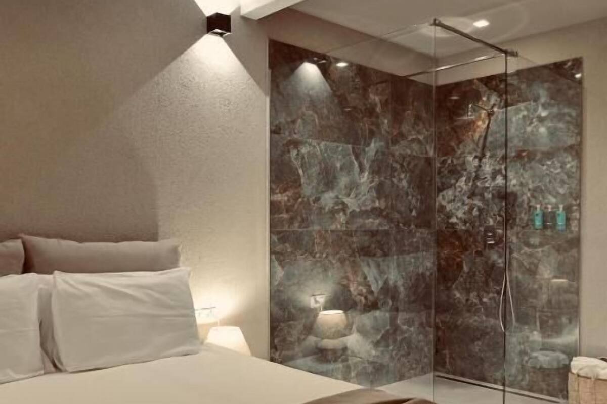 Un dormitorio moderno con una cama grande, un cerramiento de ducha de cristal y una pared de mármol.