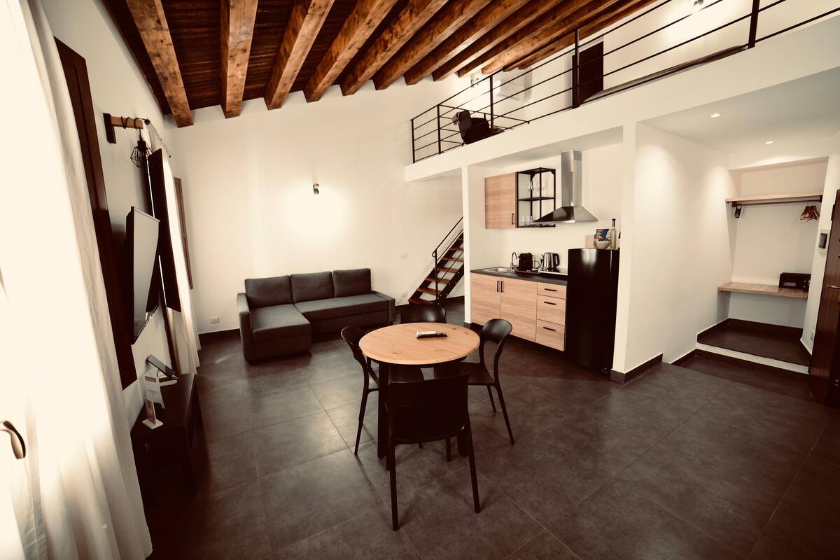 Un interior moderno con comedor, sofá, cocina y escalera.